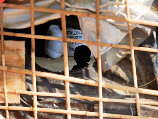 Silueta dieťaťa cez bambusové palice pokryté igelitovými vreciami - materiál provizórnych prístreškov obyvateľov tábora.