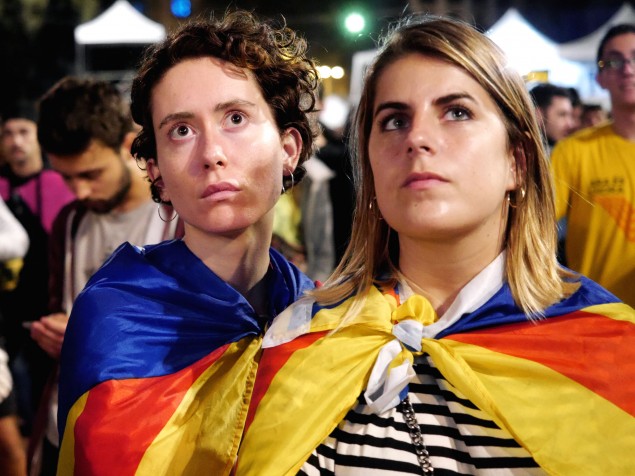 Mladé ženy neveriacky sledujú prejav španielskeho premiéra z veľkoplošnej obrazovky na námestí Catalunya.