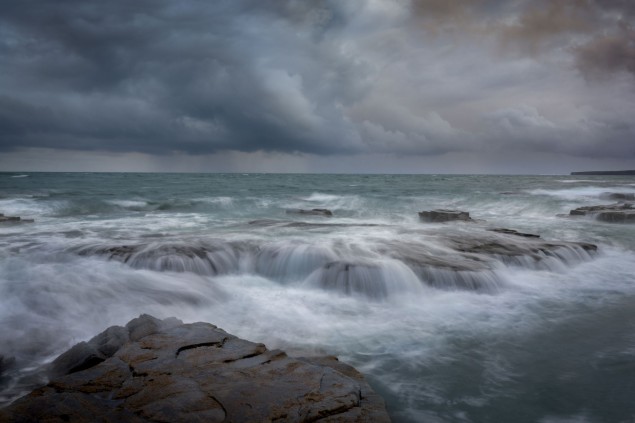 Zvoľte vhodnú rýchlosť závierky. Oceánske vlny obtekajúce skaly so sivými búrkovými oblakmi na oblohe. Foto: George Karbus @1/3 s, f/22, ISO 31, 33 mm