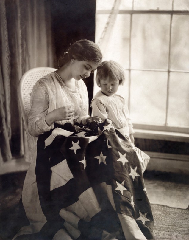 A child watches as a woman sews a star on a United States flag, 1917. PHOTOGRAPH BY MAY SMITH, NATIONAL GEOGRAPHIC